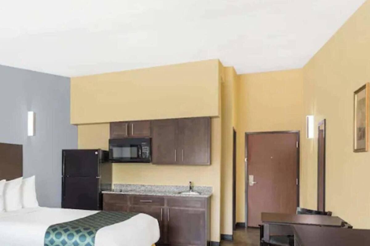 A hotel room with a bed, a kitchenette, a flat-screen TV, and a door.