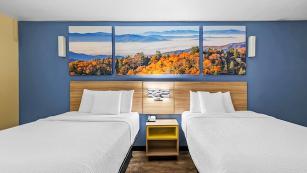 A hotel room with two beds, a wooden headboard, a nightstand with a phone, and a large landscape painting above the beds. - Days Inn by Wyndham New Orleans Pontchartrain (New Orleans)