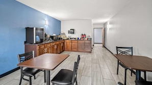 A compact kitchen with wooden cabinets, a microwave, and a coffee machine. There are two dining tables with chairs, and a small TV mounted on the wall. - Days Inn by Wyndham New Orleans Pontchartrain (New Orleans)