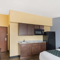 Habitación de hotel compacta con kitchenette que incluye microondas, refrigerador y armarios de madera.