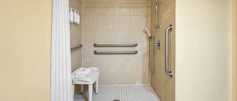 A handicap-accessible bathroom with a bench, handrails, and a shower area.