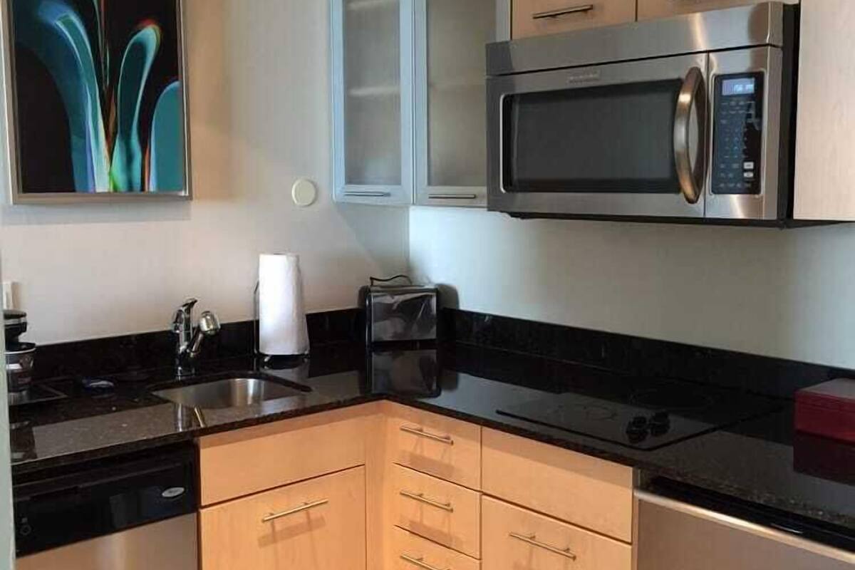 A modern kitchen with stainless steel appliances, wooden cabinets, and a black countertop.