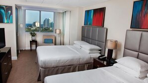 A hotel room with two beds, a TV, a desk, and a view of the city. - Gallery One Private Condos (Fort Lauderdale)