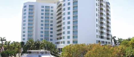A modern hotel with multiple high-rise buildings, a yacht docked in front, and palm trees in the background.