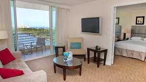 A hotel room with a sofa, a coffee table, a TV, a bed, and a balcony with a view of the city. - Gallery One Private Condos (Fort Lauderdale)