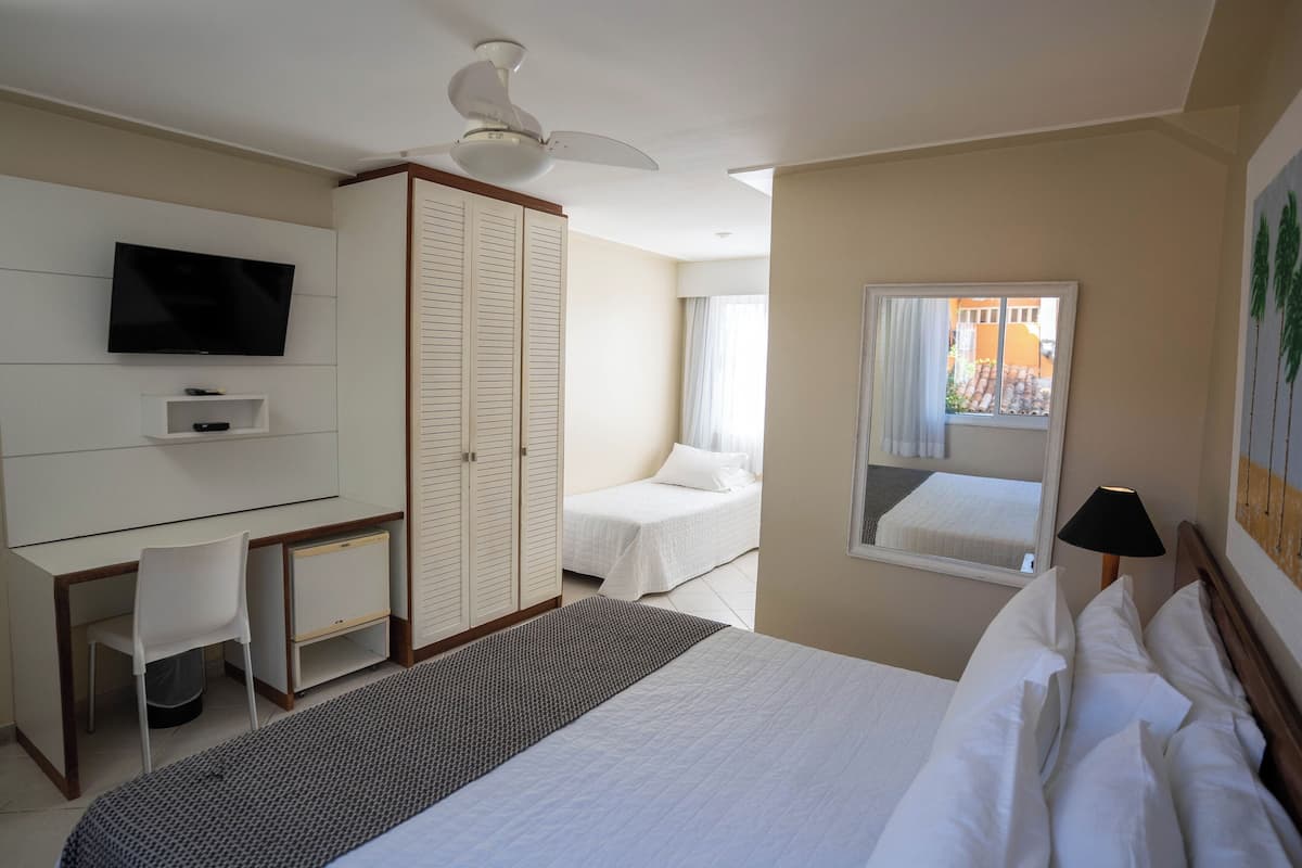 Une chambre d’hôtel comprenant un lit, un bureau avec une chaise, une télévision, une armoire et une fenêtre donnant sur l’extérieur.