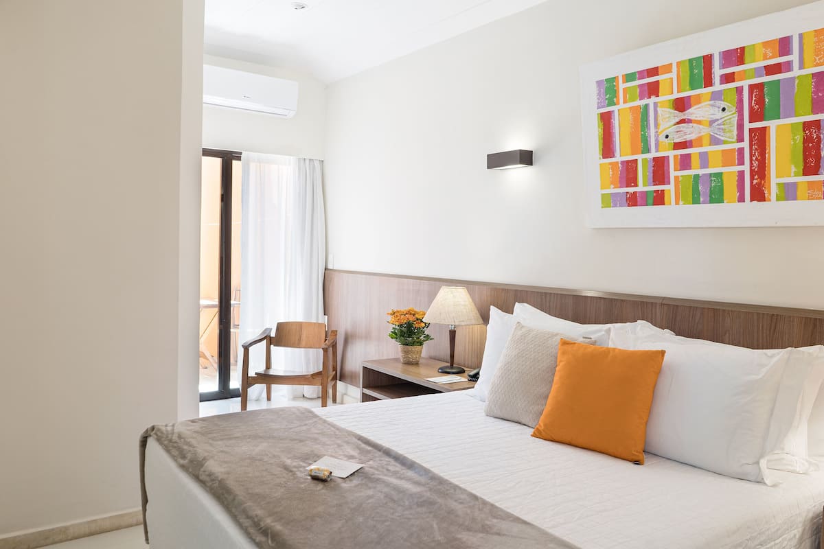 Une chambre d’hôtel avec un lit, une chaise, une table de chevet, une lampe et une œuvre d’art colorée accrochée au mur.