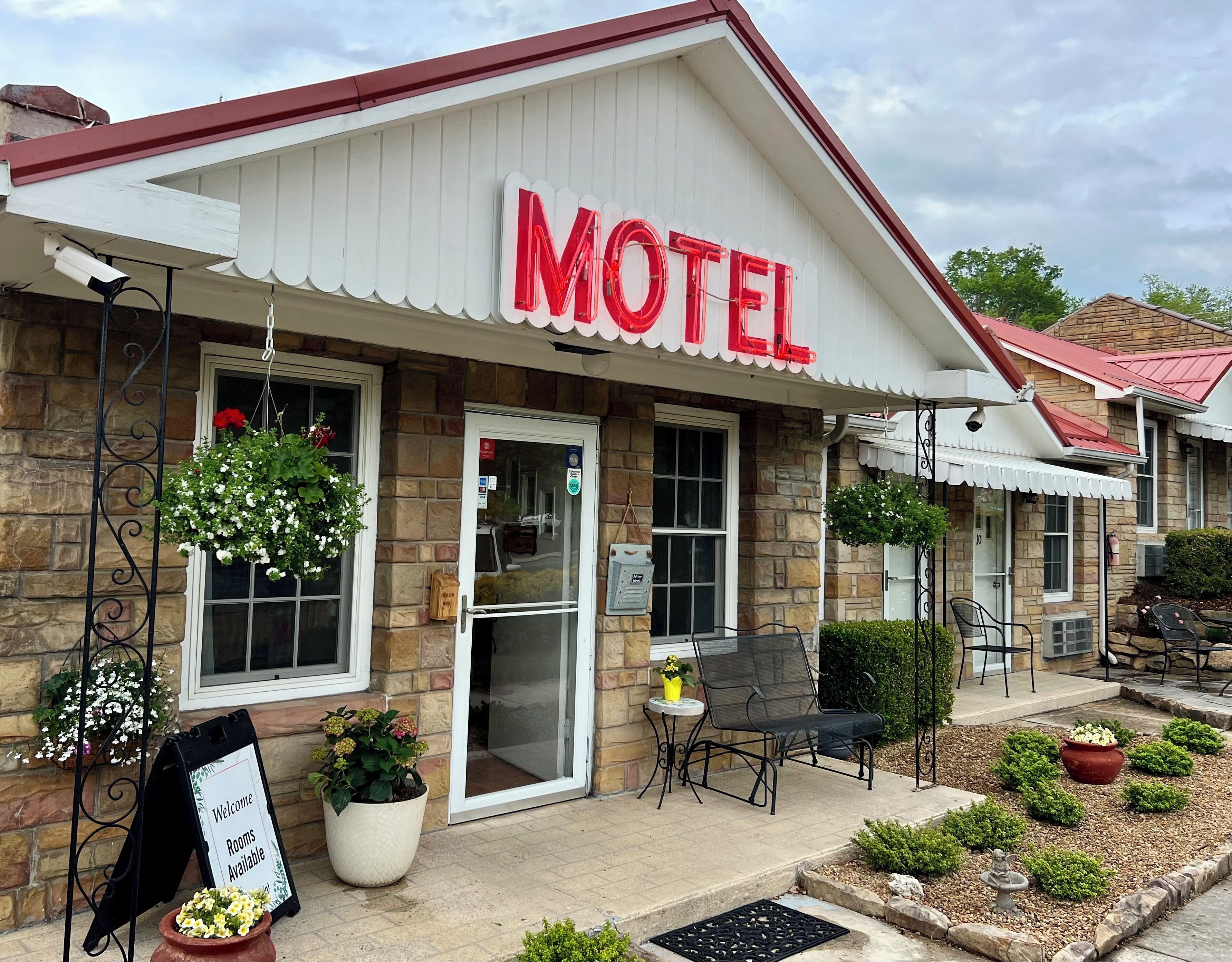 A motel with a prominent red sign, a welcoming signboard, and outdoor seating.