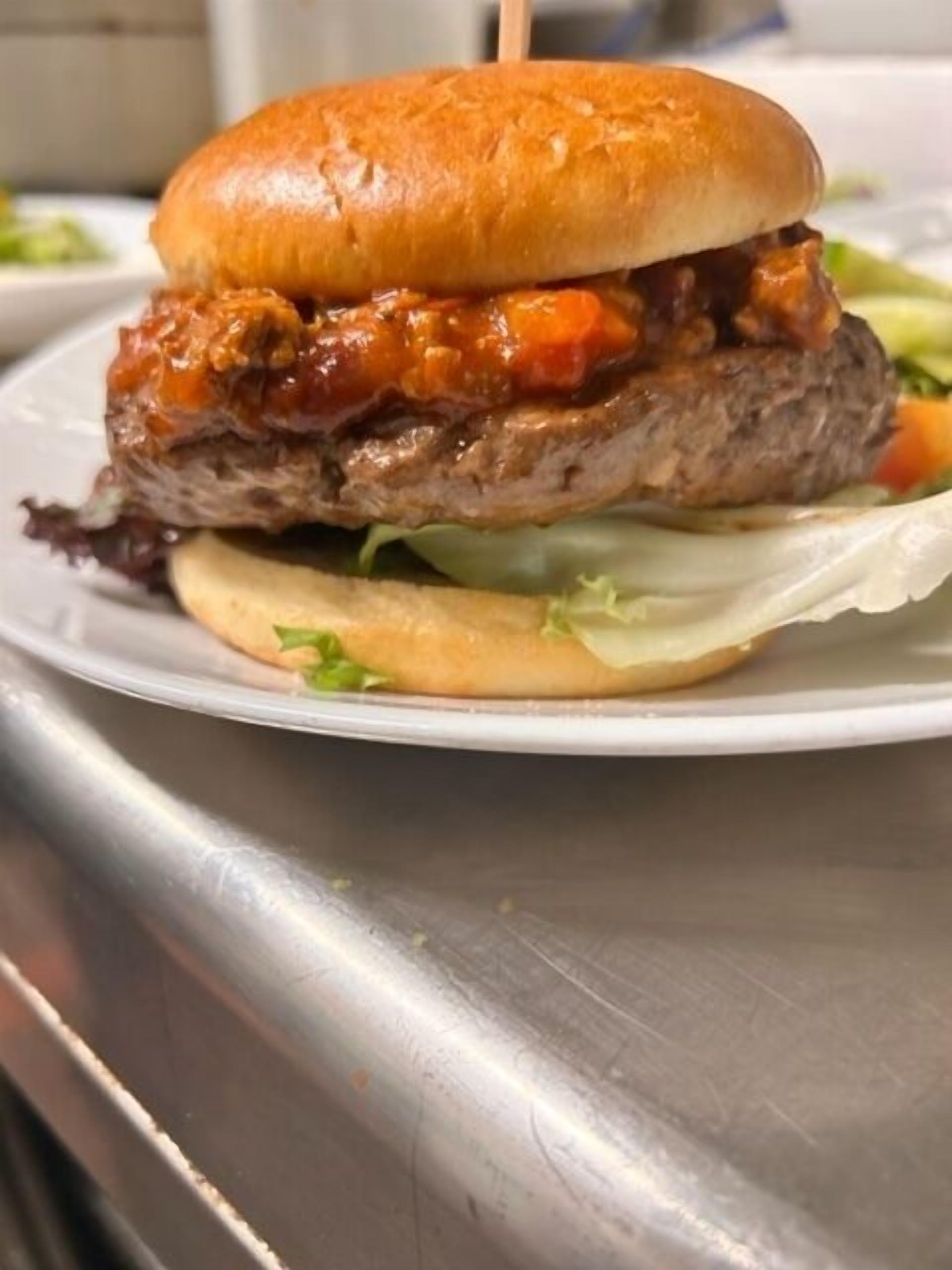 A burger with a sesame seed bun, lettuce, and a sauce topping, served on a white plate.