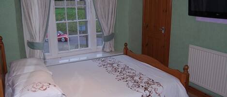 A bedroom with a single bed, a window with curtains, a door, and a television on the wall.