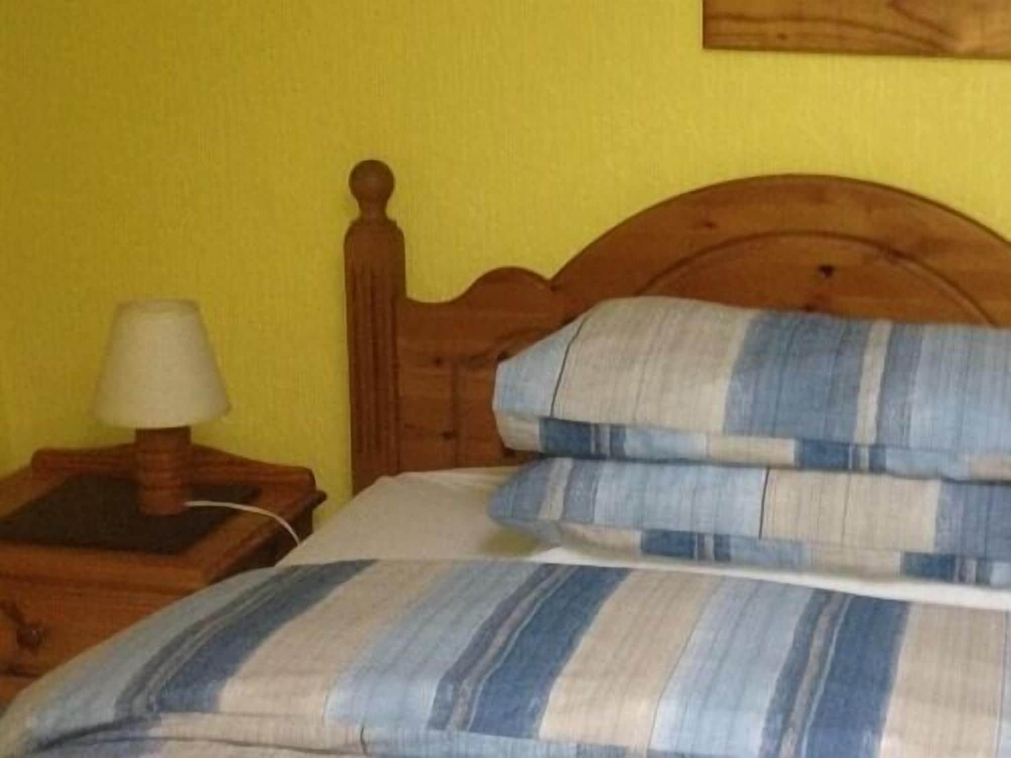 Un letto con testiera in legno, un cuscino a righe e un comodino con una lampada.