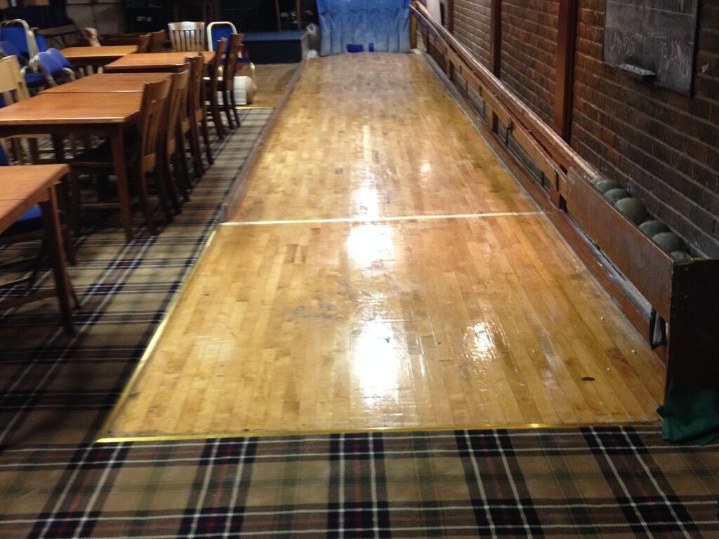 A long, narrow room with wooden flooring and a plaid carpet.