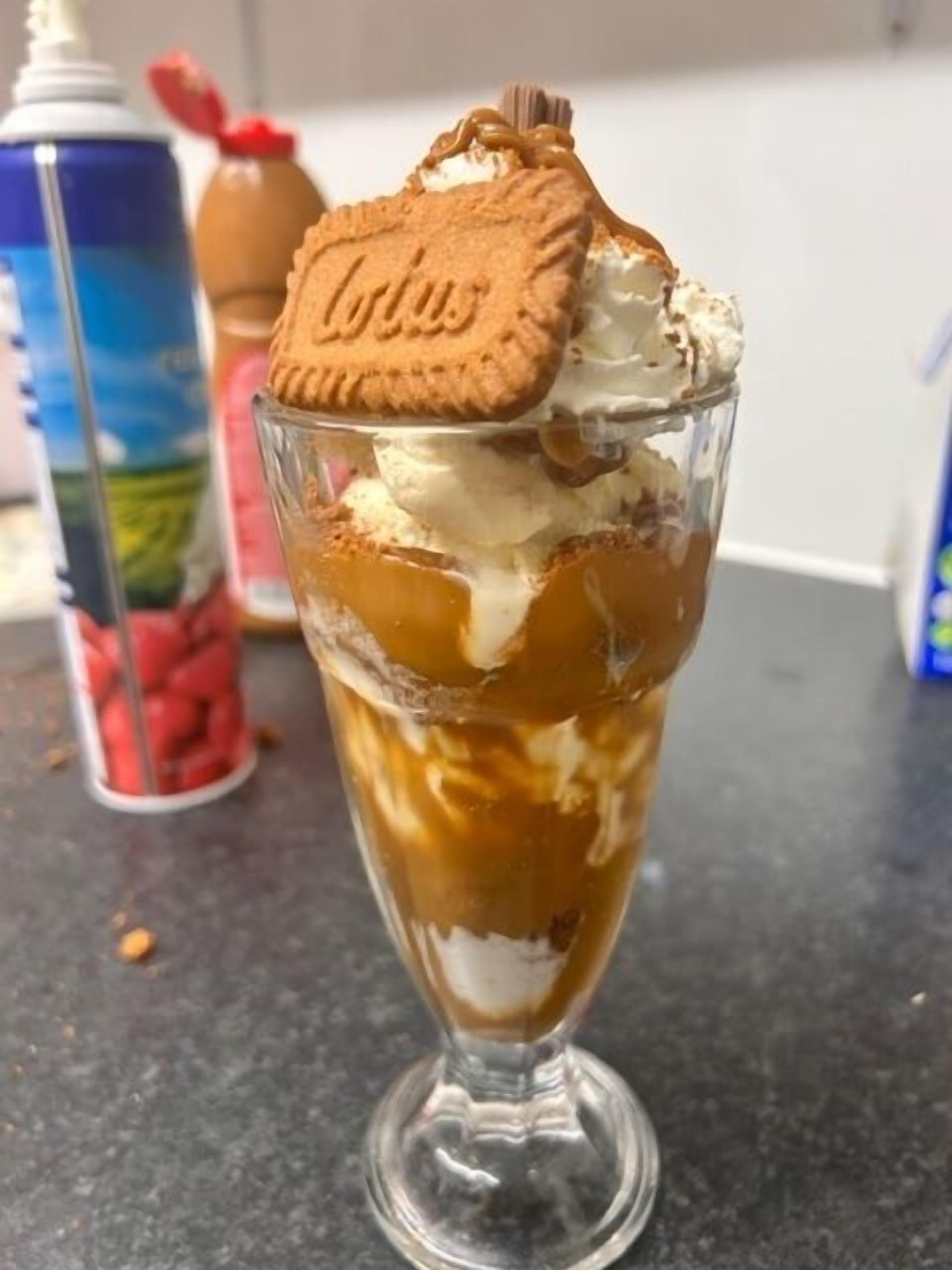 Ein Dessert in einem klaren Glas mit Schichten aus Eis und Karamellsauce, verziert mit einem Keks und einer Schokoladenecke.