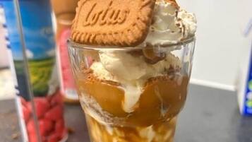 Ein Dessert in einem klaren Glas mit Schichten aus Eis und Karamellsauce, verziert mit einem Keks und einer Schokoladenecke.