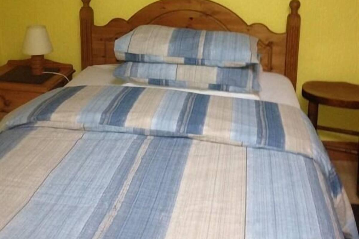 A bed with a striped bedspread, a wooden headboard, a nightstand with a lamp, and a small table.