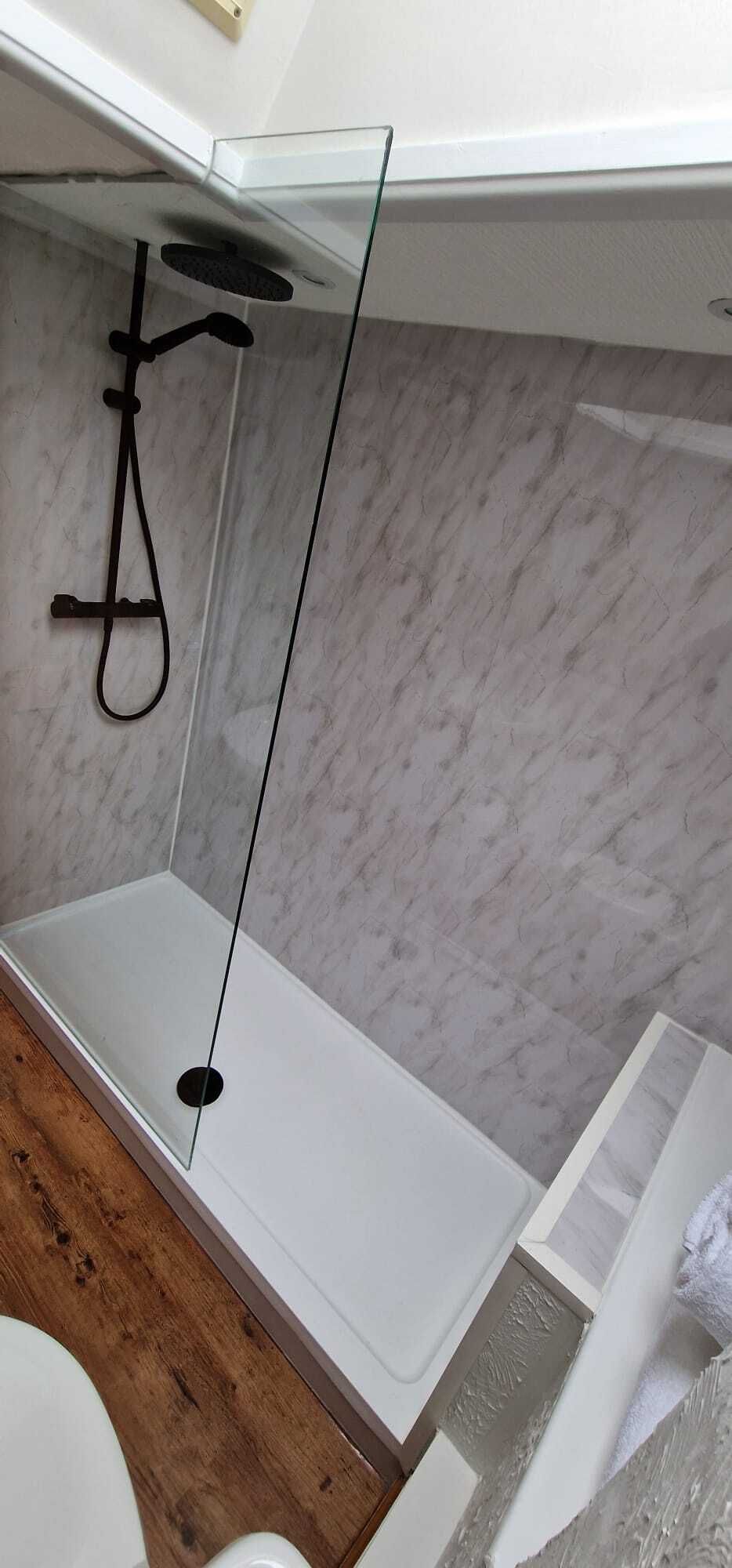 Un baño con una bañera blanca, una ducha con mampara de vidrio y una pared de mármol.