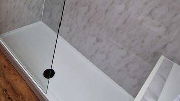Un baño con una bañera blanca, una ducha con mampara de vidrio y una pared de mármol.
