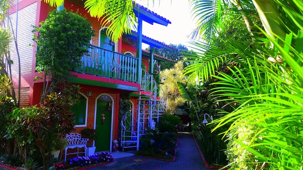 A colorful building with a green door, a balcony, and a garden area with plants and a bench.