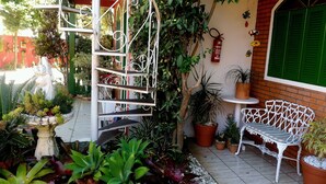 Uma área de jardim com uma escada espiral de metal branco, plantas em vasos, um banco de metal branco e um extintor de incêndio na parede.