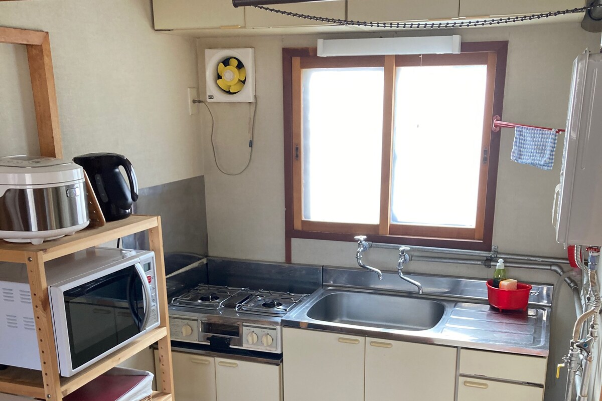A compact kitchen with a microwave, stove, sink, and wooden shelves.