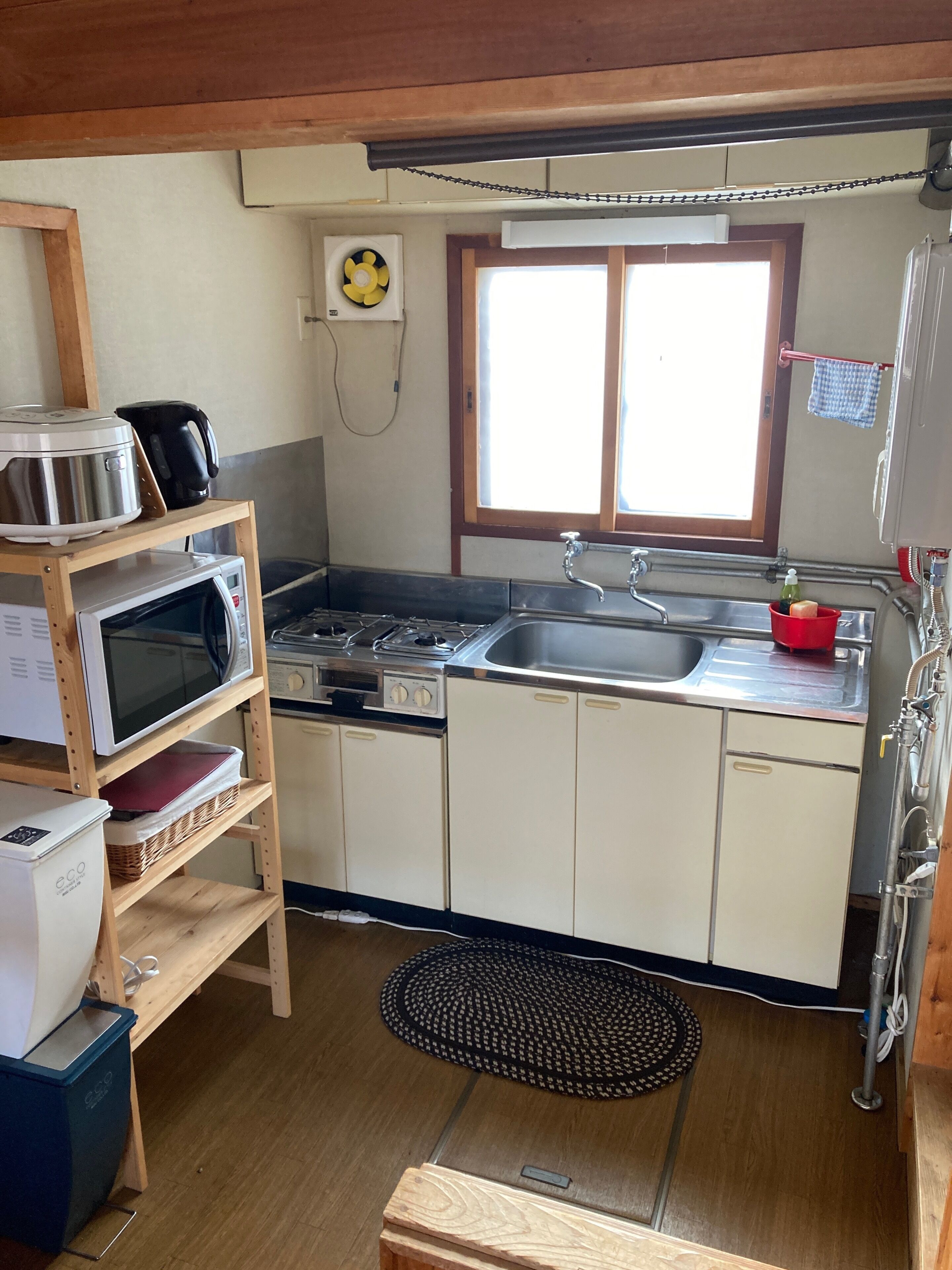 Une cuisine compacte équipée d’un four à micro-ondes, d’une cuisinière, d’un évier et d’étagères en bois.