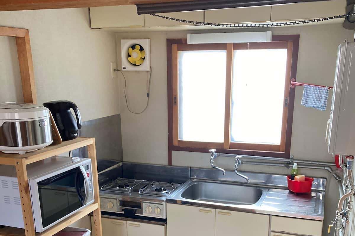 A compact kitchen with a microwave, stove, sink, and wooden shelves.
