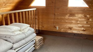 A loft bedroom with a sloped ceiling, wooden walls, a bed with white bedding, and two skylights. - Niseko Cottage Akagera (Kutchan)