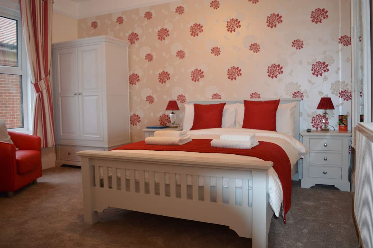 Quarto bem arrumado com cama, mesa de cabeceira, cadeira e guarda-roupa.