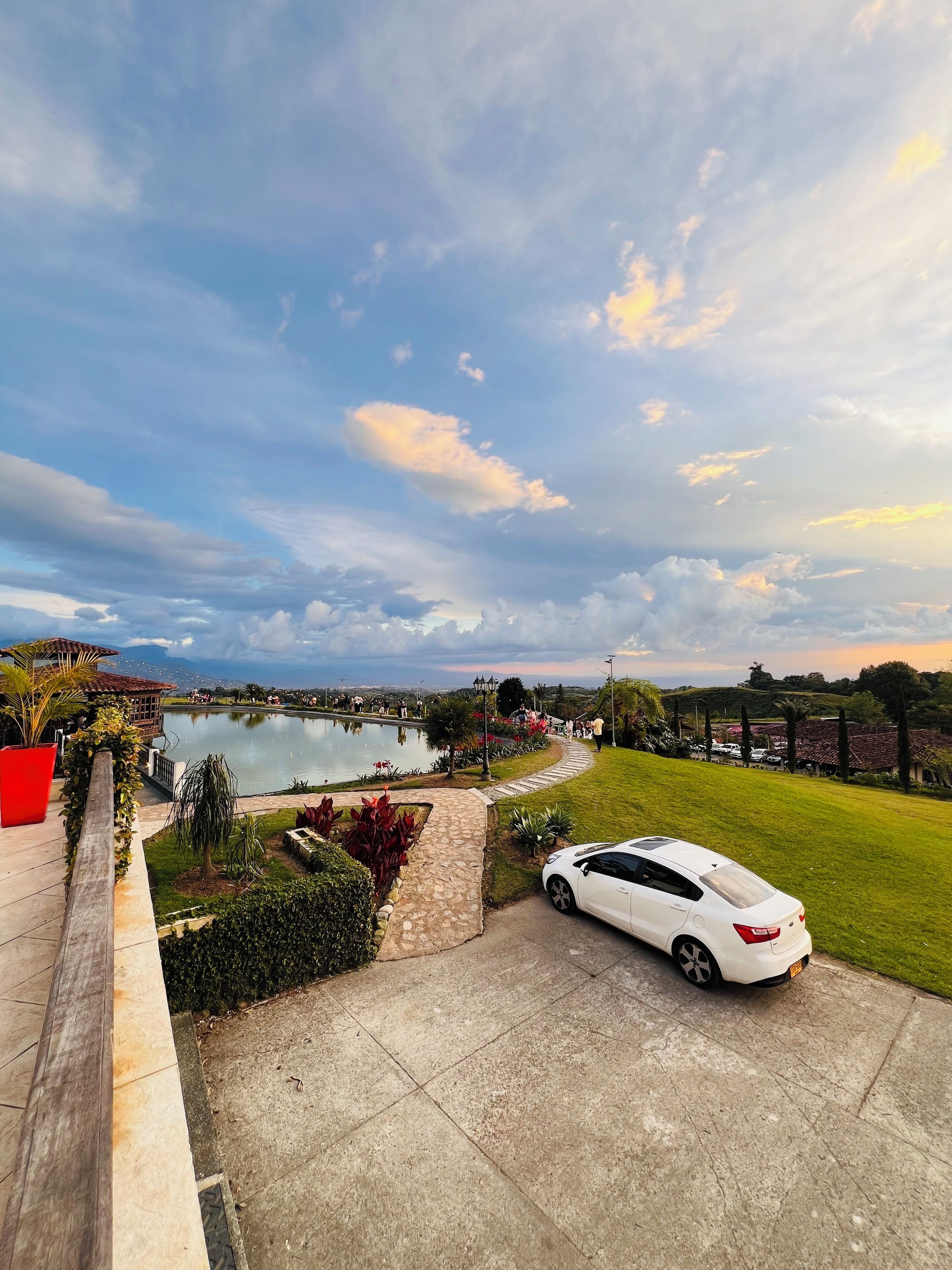 A white car parked in a driveway with a view of a lake and a garden.