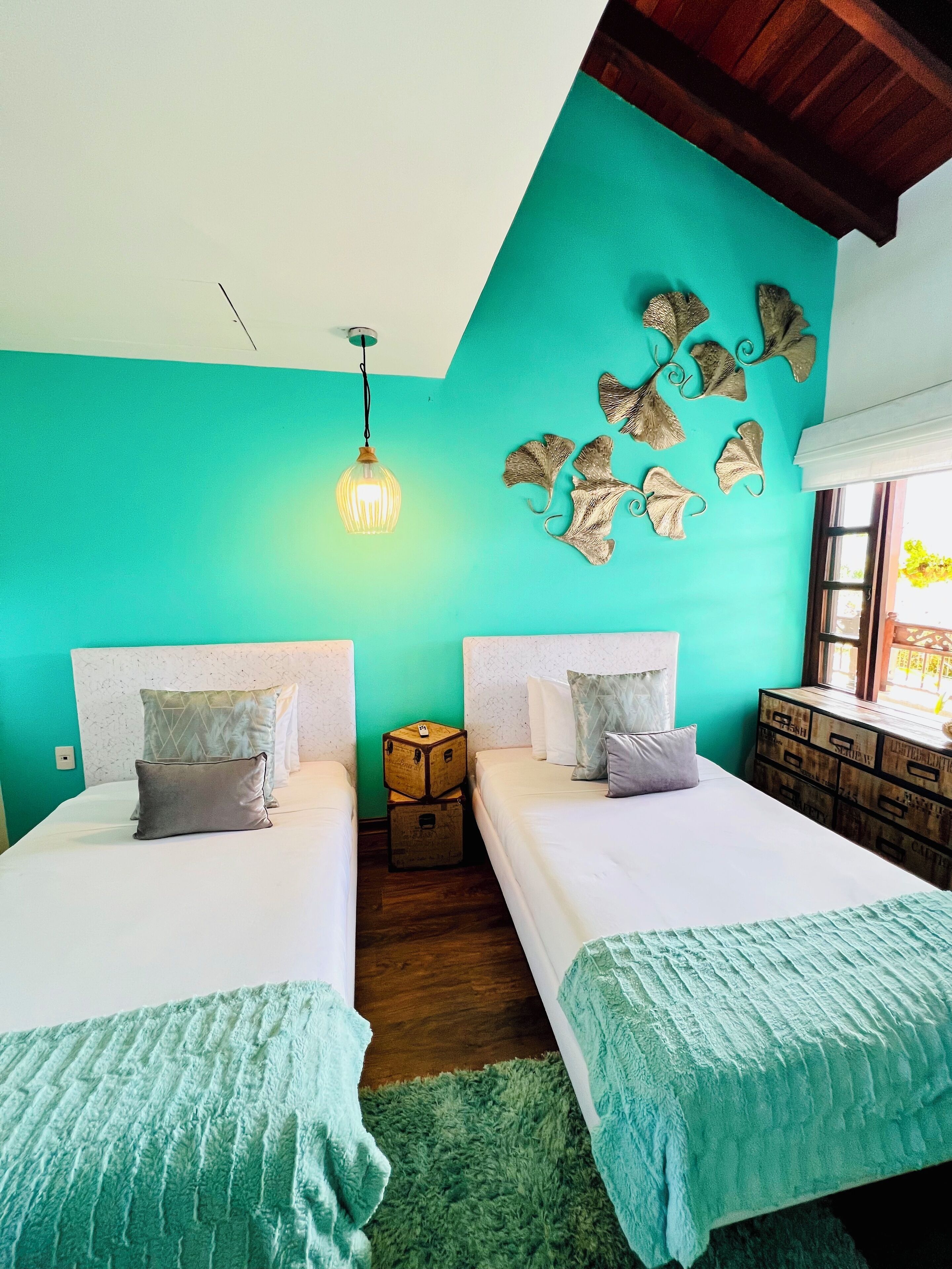 Una habitación con dos camas, una pared verde azulado, techo de madera y una obra de arte de hojas decorativas.