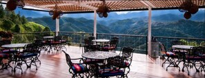 Una terraza al aire libre con mesas y sillas, con vistas a un paisaje montañoso.