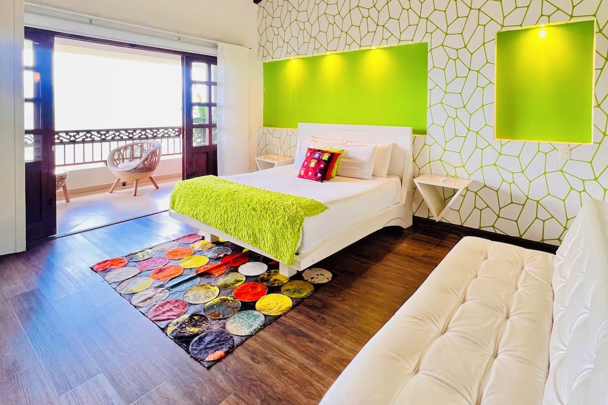 Une chambre moderne avec un plafond en bois, un lit doté d’une tête de lit verte, un tapis coloré et un canapé blanc.