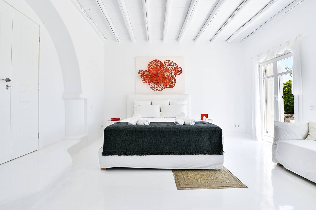 A modern bedroom with a large bed, white walls, and a red abstract artwork above the bed.