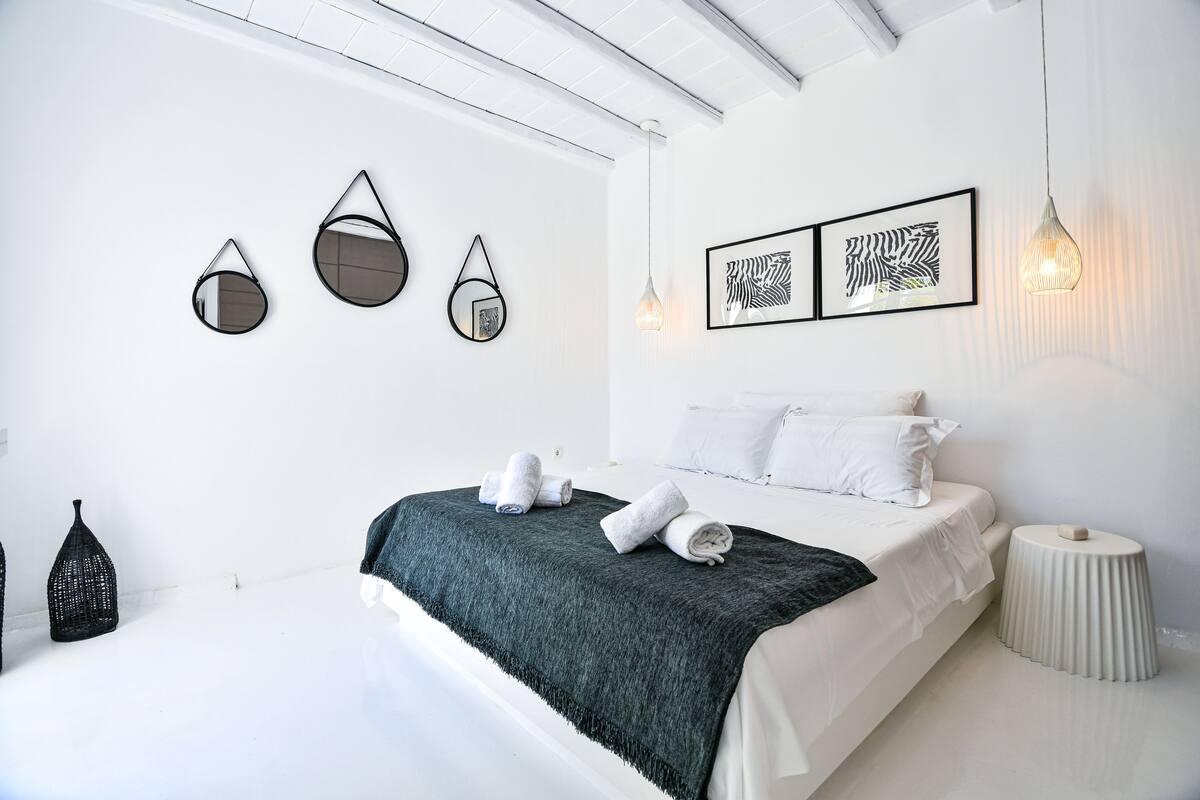 A modern bedroom with a bed, decorative mirrors, and framed artwork on the wall.