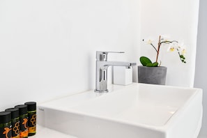A white bathroom sink with a chrome faucet, a potted orchid, and several bottles of olive oil. - The One Mykonos (Mykonos)
