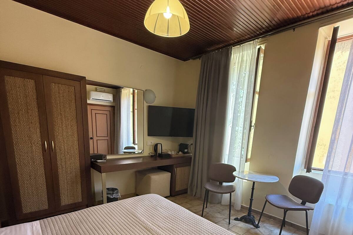 A hotel room with a bed, a desk, a chair, a small table, a television, and a wardrobe.