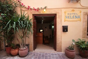 The entrance to Hotel Helena with a wooden door, potted plants, and a sign above the door.