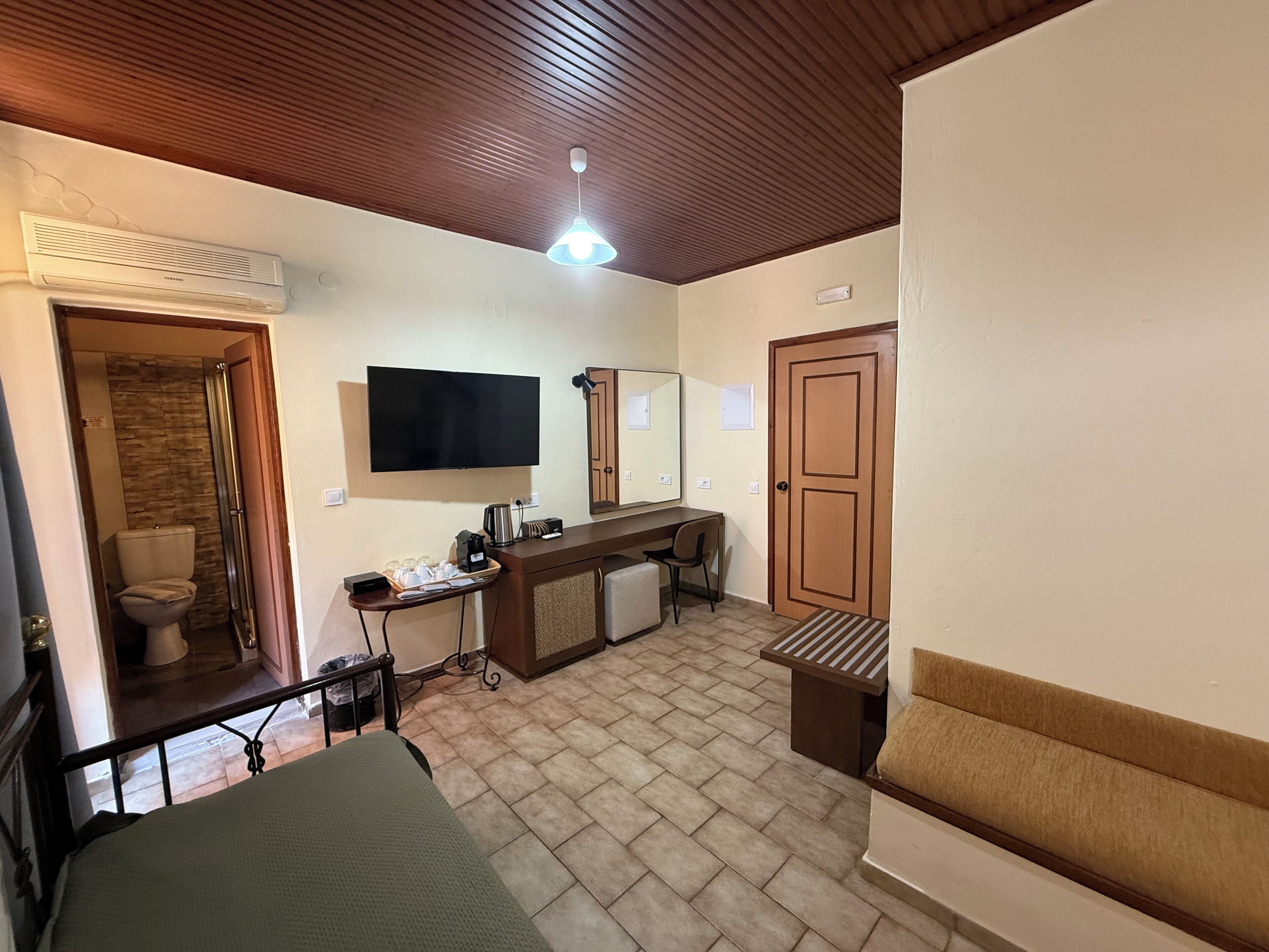 A hotel room with a bed, a desk with a chair, a television, a mirror, and a door.