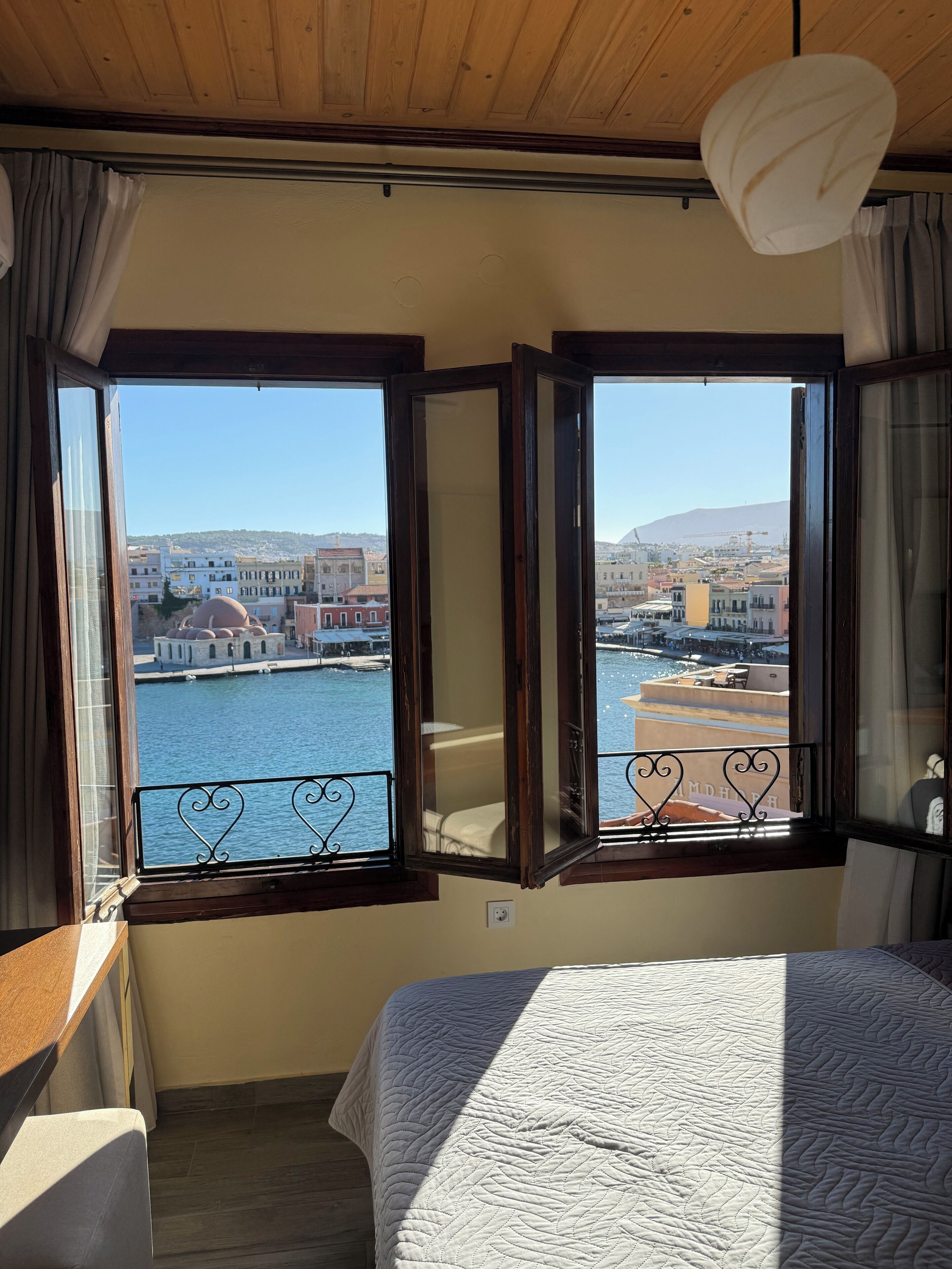 A room with a bed, a view of a body of water, and a cityscape in the background.