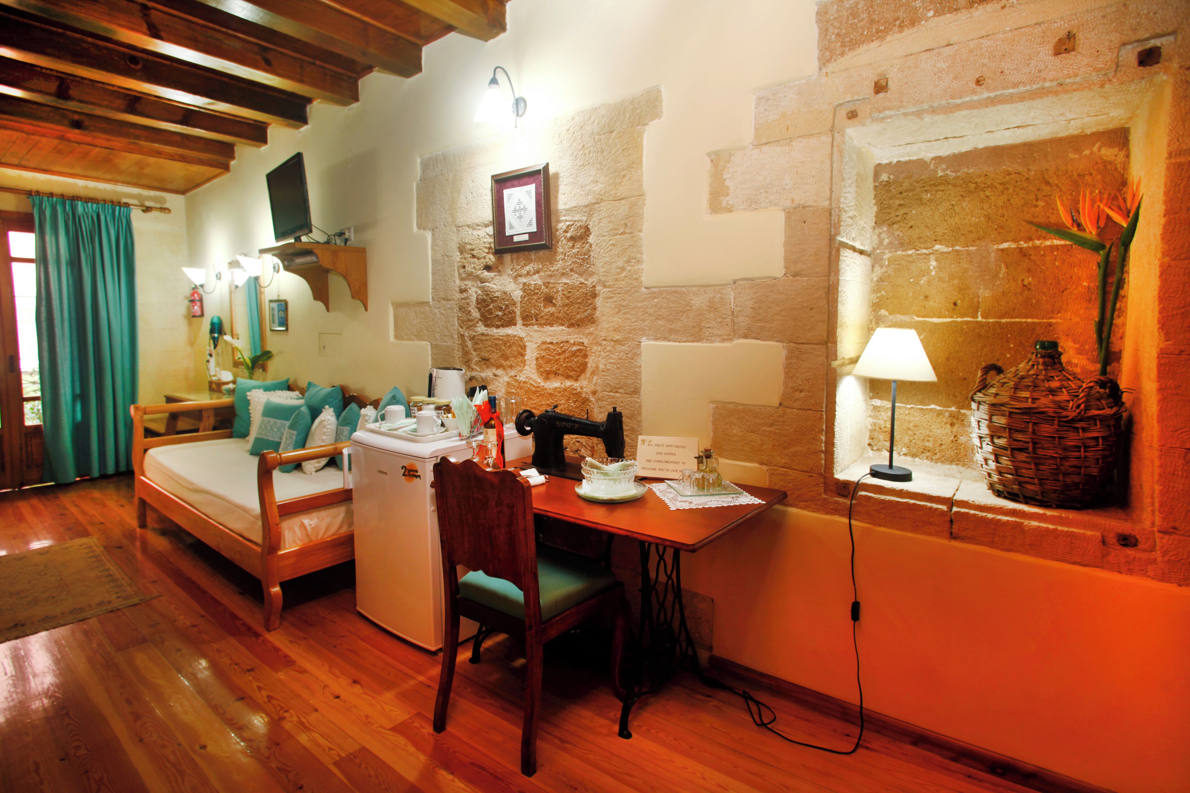 A cozy room with a bed, a small table, a chair, a sewing machine, and a window with a plant.