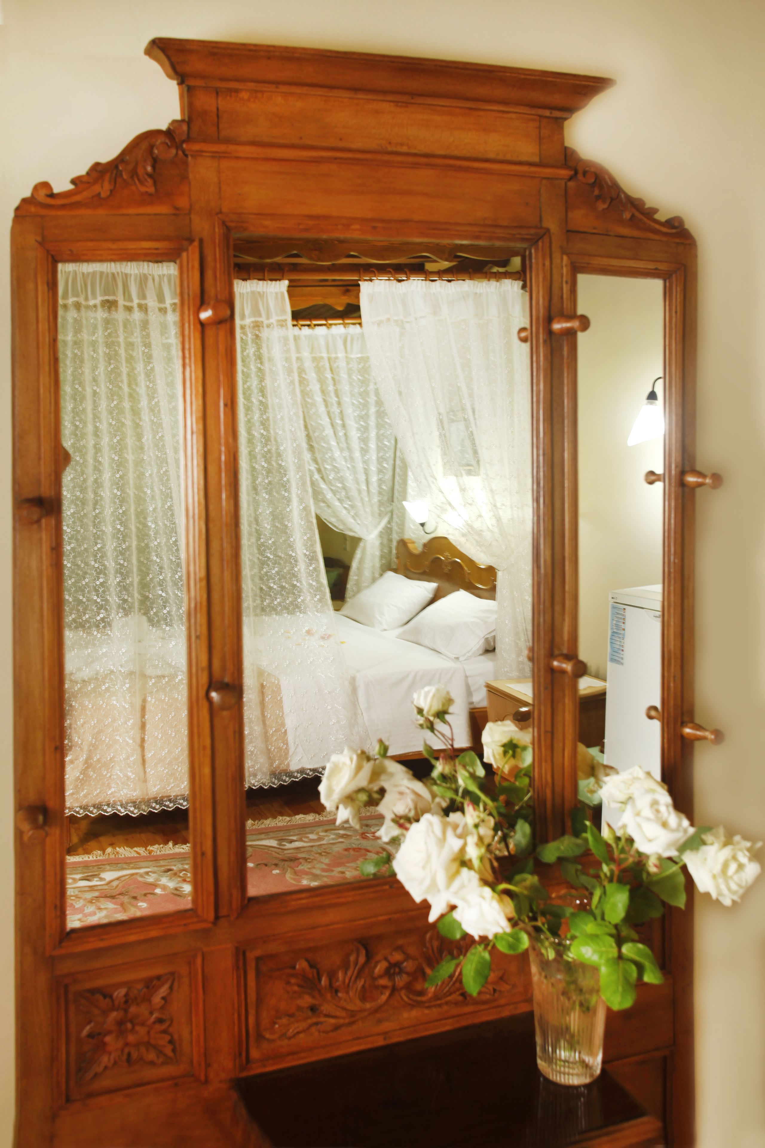 A wooden armoire with a mirror, a bed with white bedding, and a vase with white flowers.