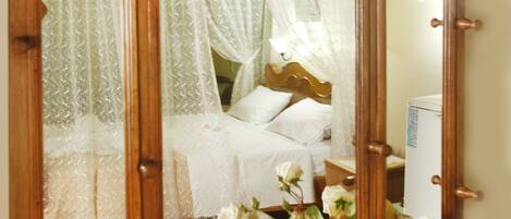 A wooden armoire with a mirror, a bed with white bedding, and a vase with white flowers.