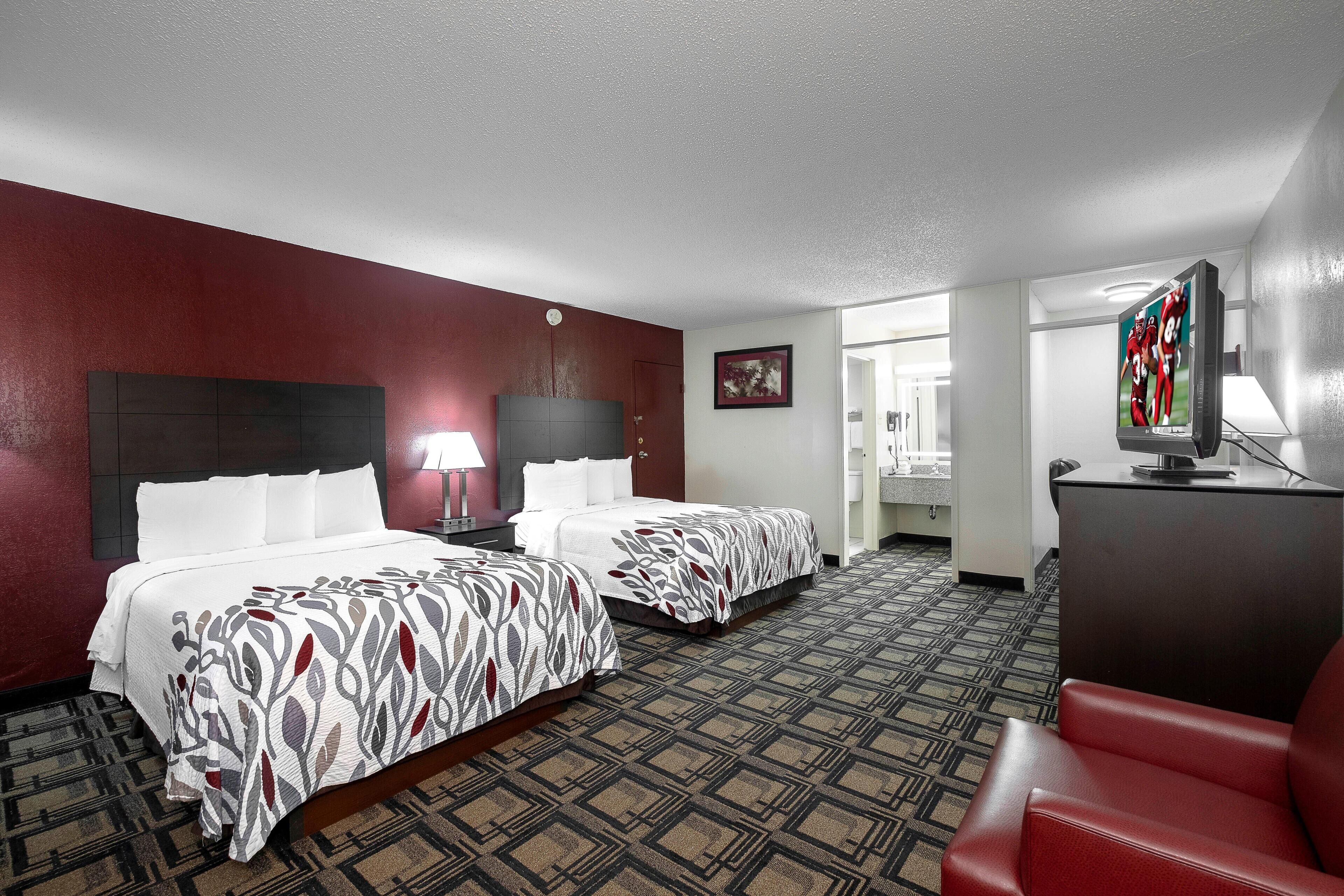 A hotel room with two beds, a TV, a desk, and a chair.