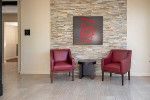 Vestíbulo de hotel con dos sillones de cuero, una mesita redonda y una pared de piedra con el logotipo de Red Roof Inn.