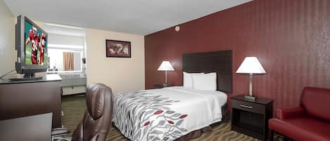 A hotel room with a bed, two bedside lamps, a desk with a TV, a chair, and a red couch.