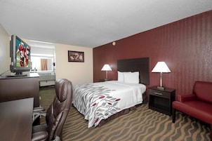 Habitación de hotel con cama, dos lámparas de noche, un escritorio con televisor, una silla y un sofá rojo.