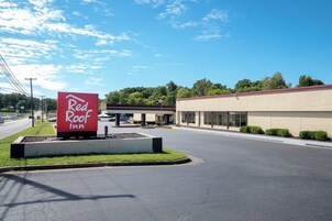 Señal de Red Roof Inn con un estacionamiento y un edificio al fondo.