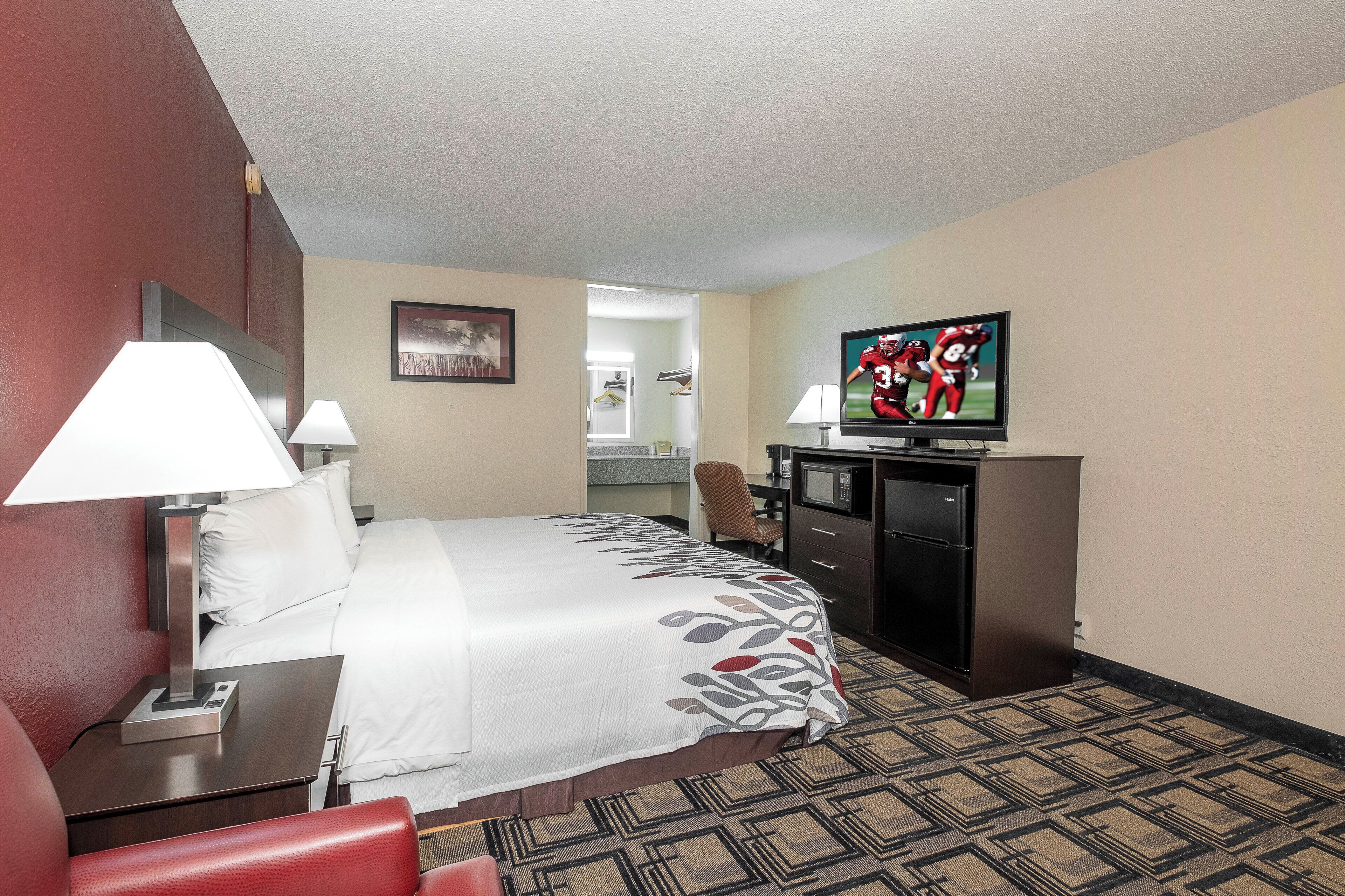 A hotel room with a bed, a desk, a television, and a kitchenette.