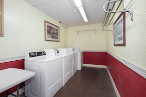 A laundry room with a white washing machine, a drying rack, and a red wall.
