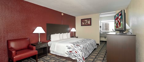 Une chambre d’hôtel avec un lit, un bureau, une chaise, une télévision et une salle de bain visible à travers une porte ouverte.